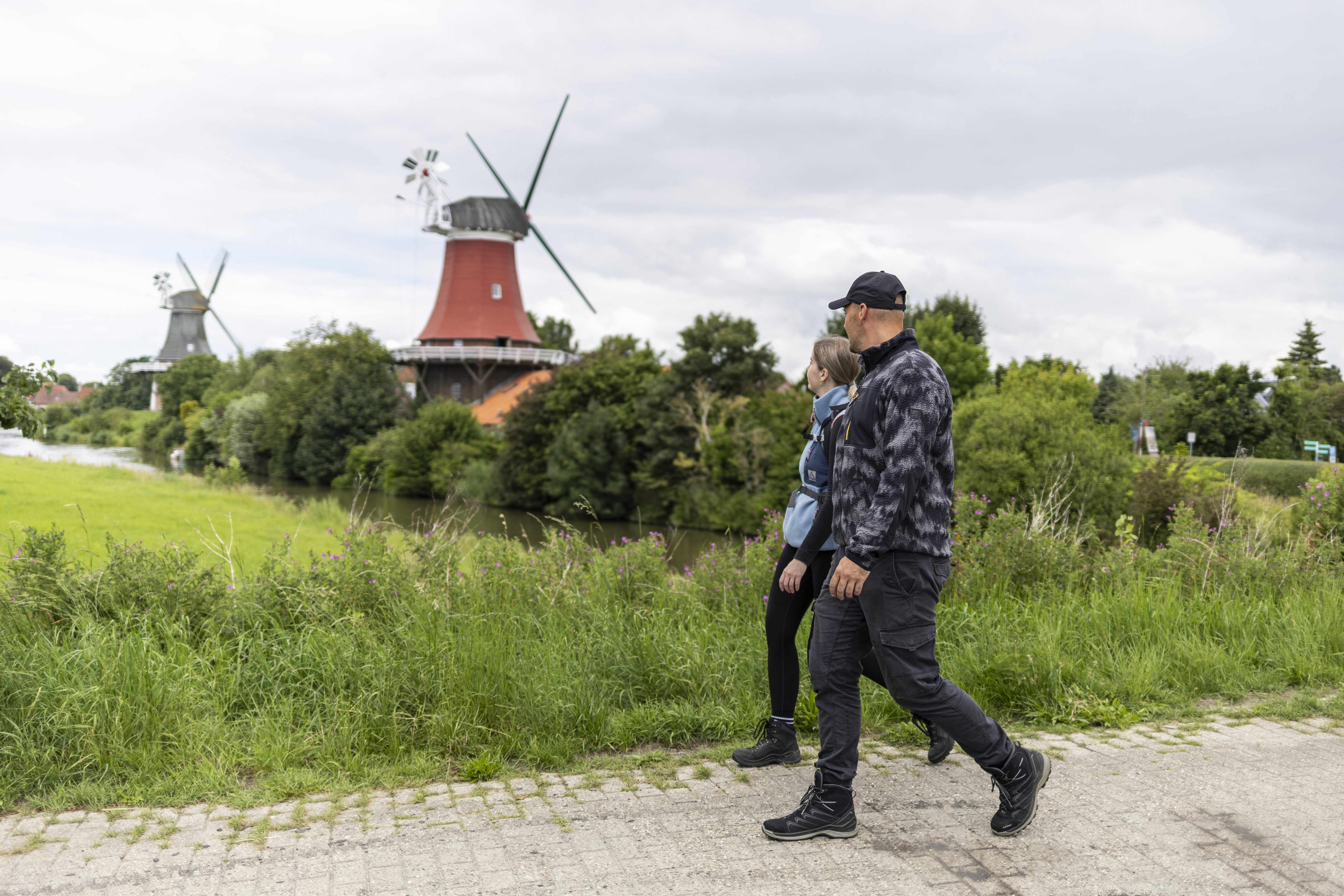 Frau und Mann wandern in Greetsiel an den Zwillingsmühlen am Kanal Krummhörn