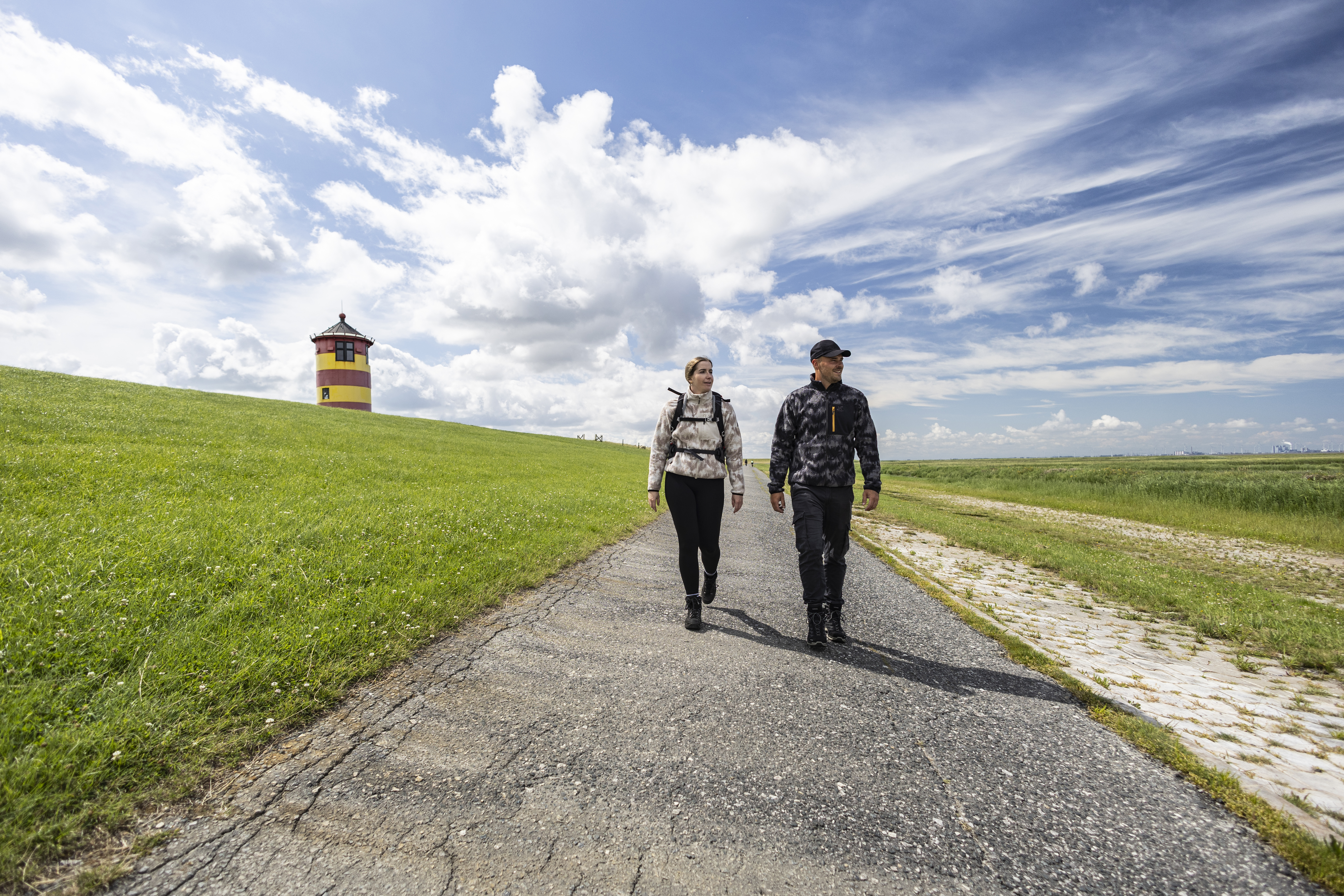 Ein Mann und eine Frau wandern am Pilsumer Leuchtturm in Ostfriesland