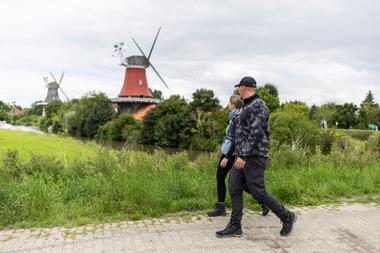 Frau und Mann wandern in Greetsiel an den Zwillingsmühlen am Kanal Krummhörn