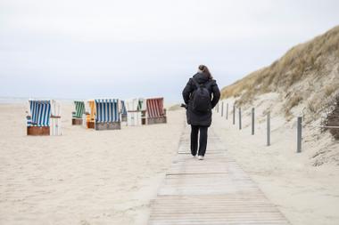 Frau spaziert auf Holzbohlenweg zwischen Dünen und Strandkörben am Strand Baltrums