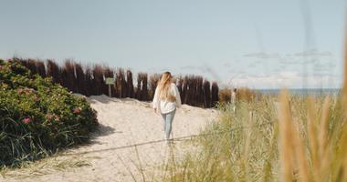 Frau spaziert entlang der Dünen zum Strand