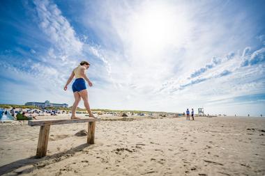 Frau balanciert auf einer Holzbank am Strand von Juist