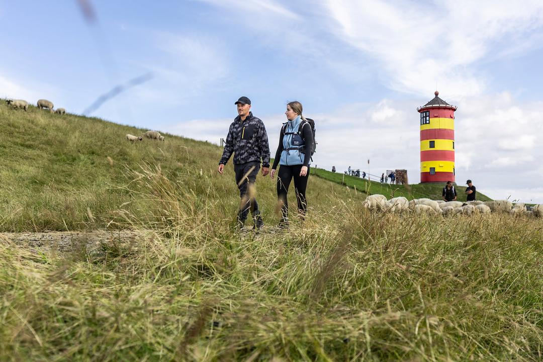 Ein Mann und eine Frau wandern am Deich am Pilsumer Leuchtturm in Ostfriesland